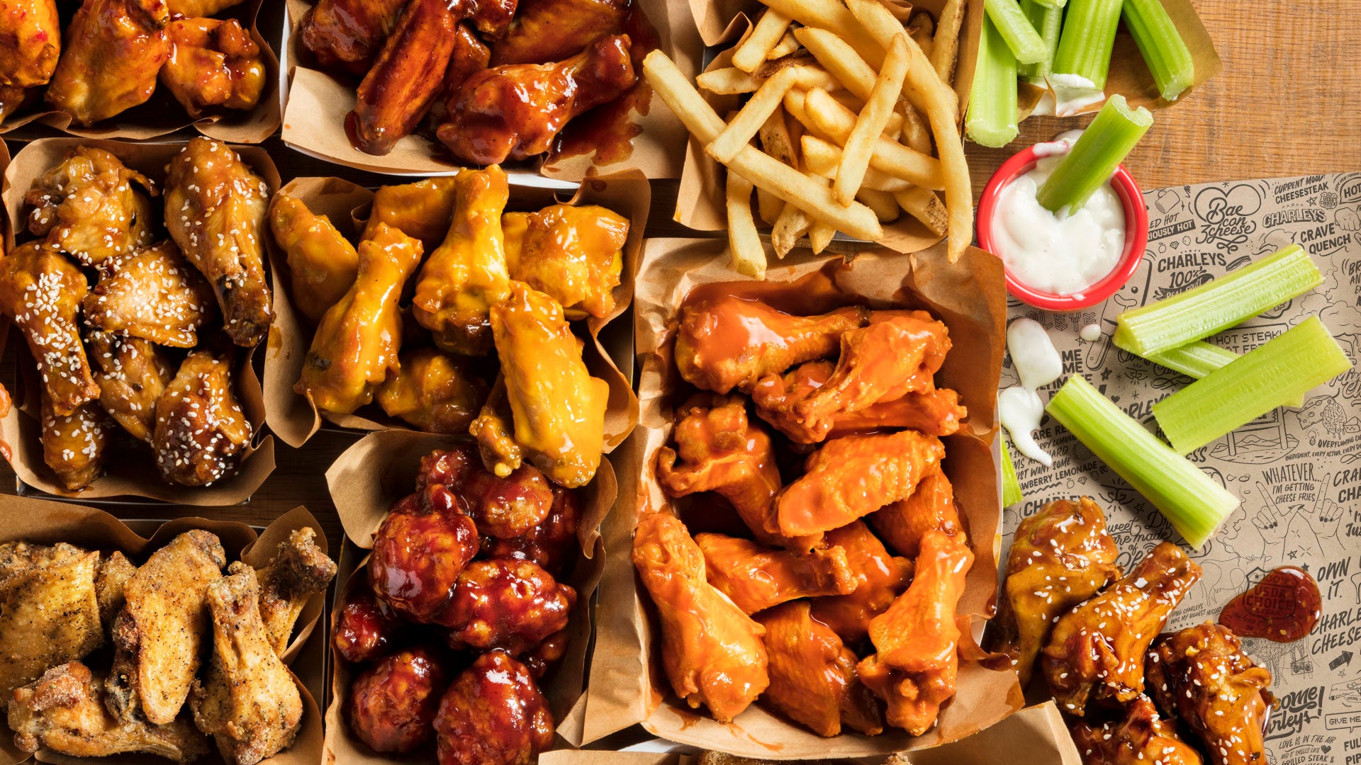 A spread of boneless and classic wings with dips on a wooden table.