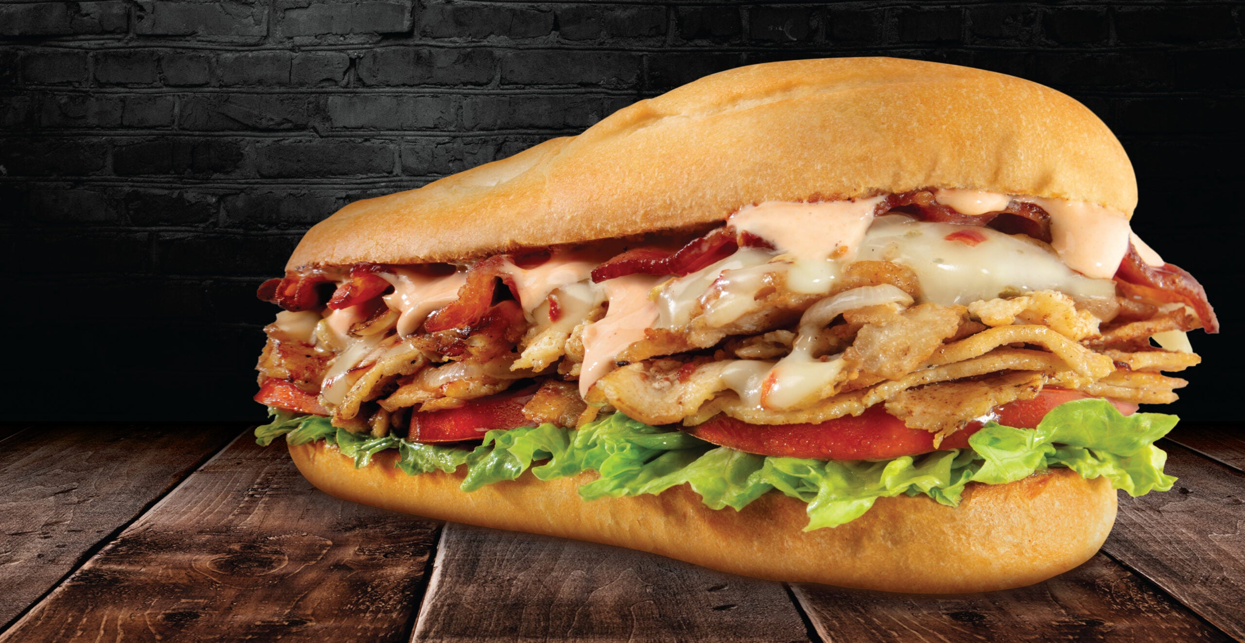 The Bacon Chipotle Cheesesteak from Charleys on a wooden table with chipotle sauce